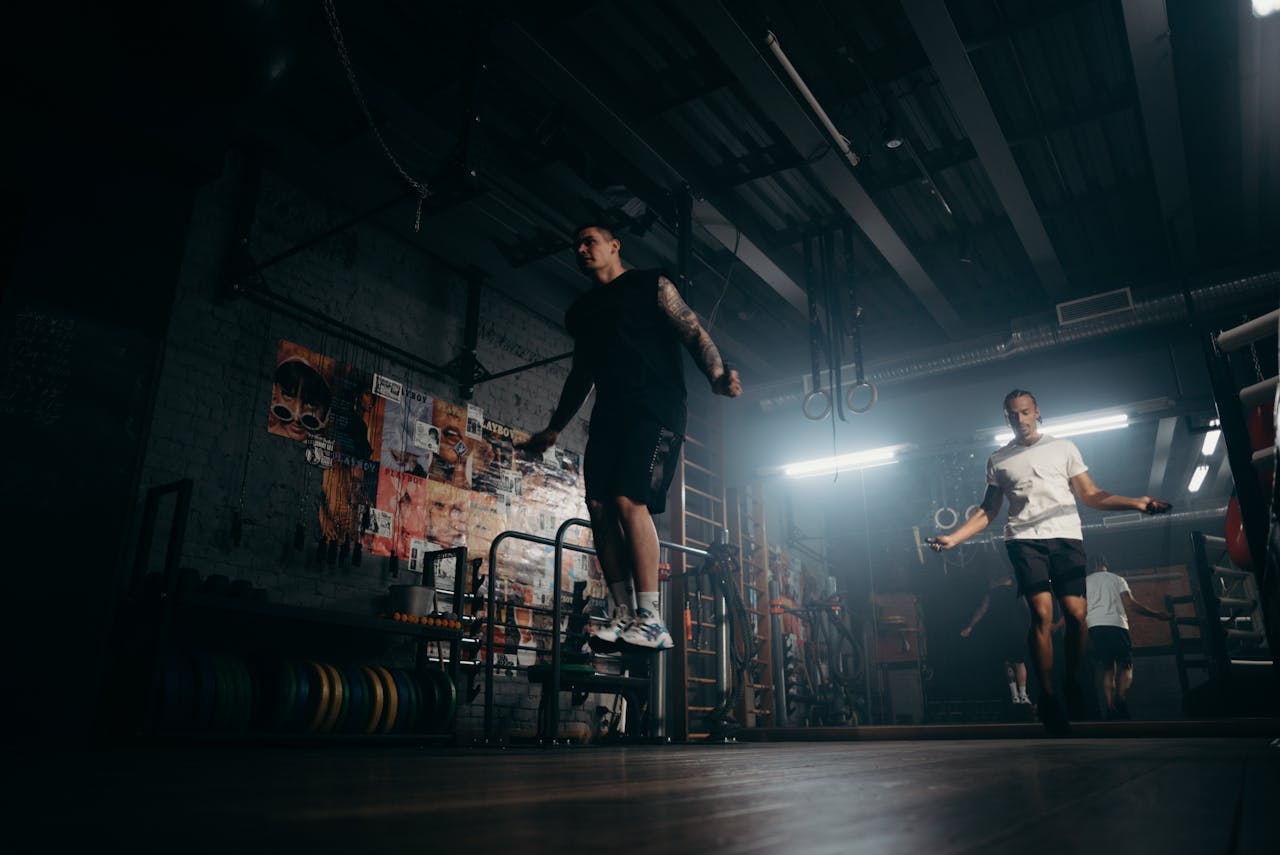 services-03 Two men actively skipping jump ropes in a dimly lit gym environment.
