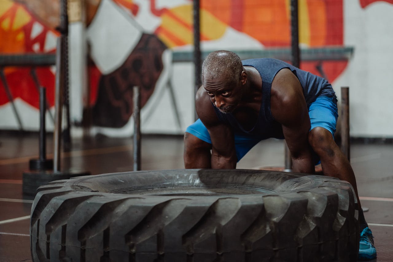 about-01 An athletic man engaged in a strength workout, flipping a large tire in a gym.
