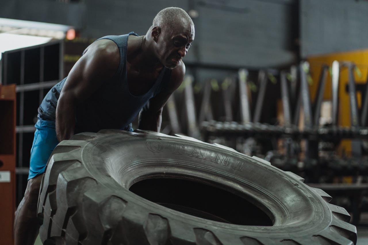 services-01 Muscular man performing tire flip exercise in a gym, showcasing strength and determination.